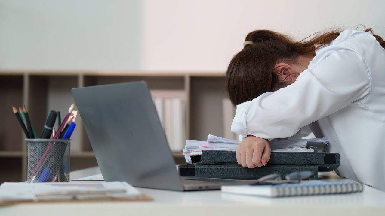 Une femme au bureau, épuisée, repose sa tête sur le bureau, illustrant la fatigue liée au stress professionnel.