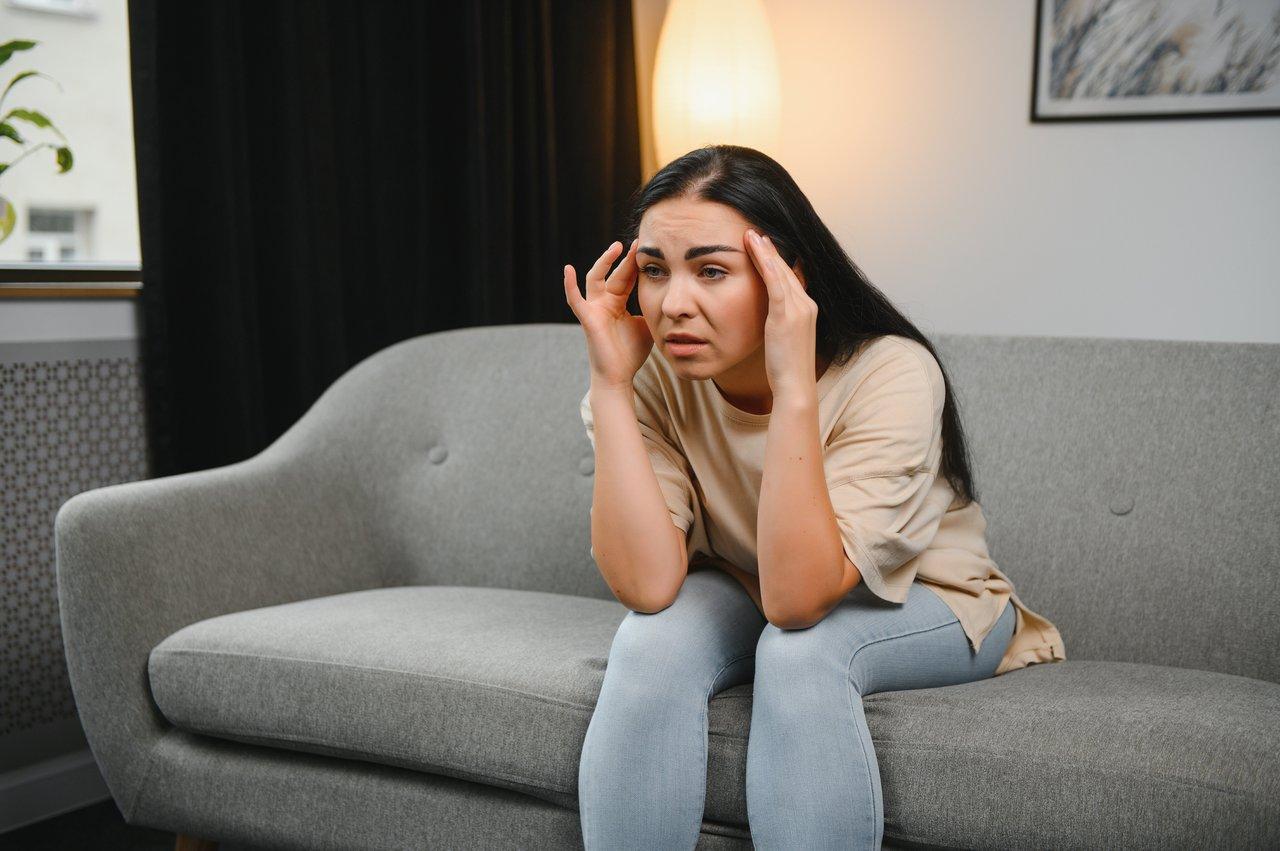 Une femme souffre de migraine dans une pièce sombre, portant des lunettes anti-lumière pour soulager la douleur.