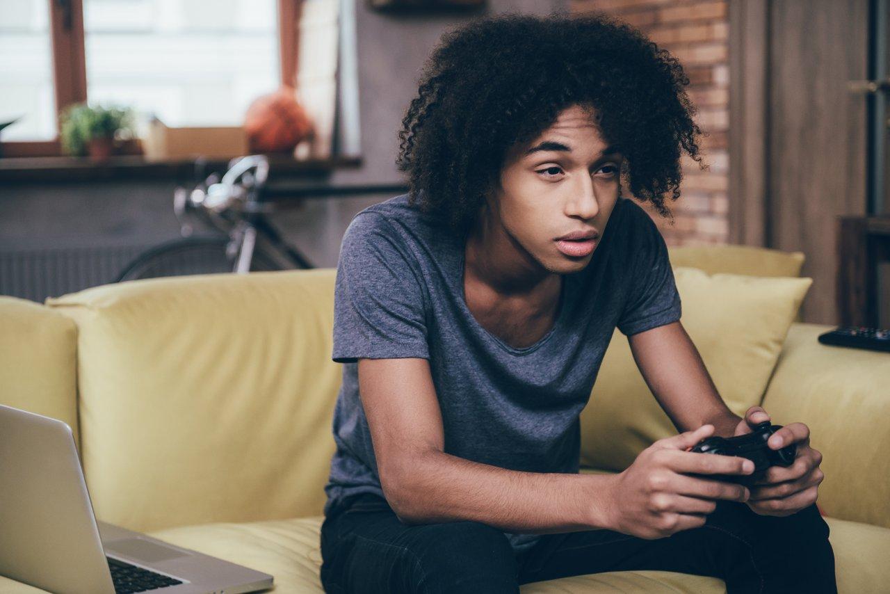 Jeune homme africain, visage préoccupé, joue intensément aux jeux vidéo, illustrant la teen video game addiction.